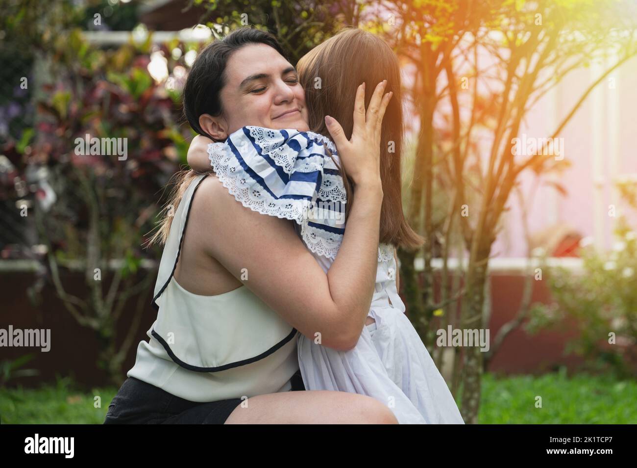 Die hispanische Mutter umarmt ihre Tochter im Hintergrund des Parks Stockfoto