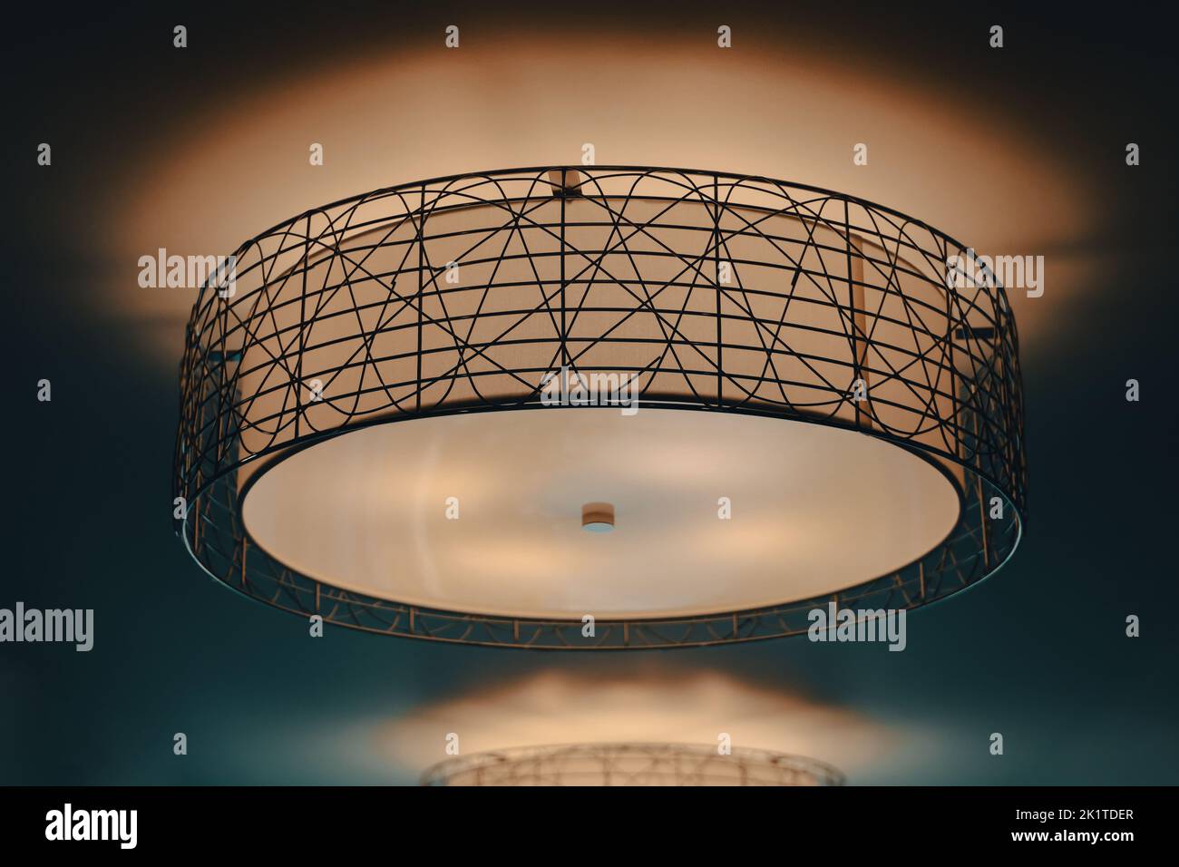 Eine leuchtende und beleuchtete Trommelleuchte mit schwarzen Metallakzenten an einer warmen Decke Stockfoto