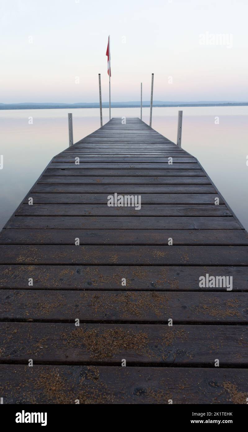 Ein Dock in den frühen Pastelltönen der Morgendämmerung, Sommer magischen Minimalismus auf einem See der perfekten Ruhe. Stockfoto