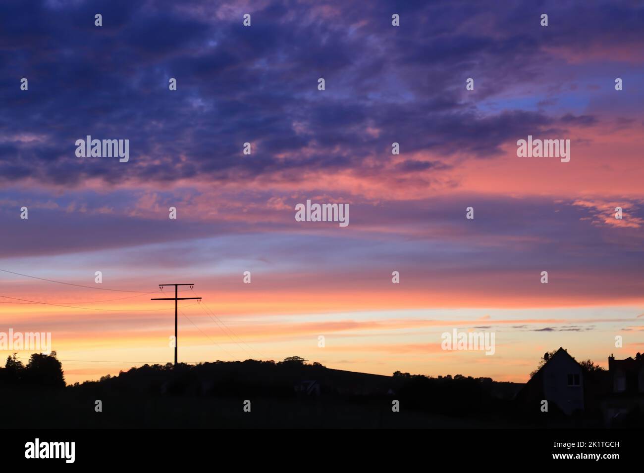 Düsterer Sonnenuntergang in einer ländlichen Landschaft mit der Silhouette eines Strompylons Stockfoto
