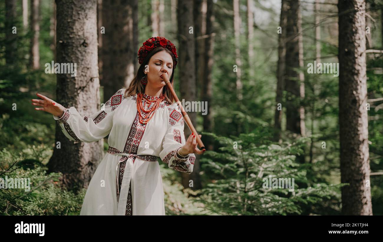 Junge Frau, die auf Holzflöte spielt - ukrainische Telenka oder Tylynka auf Waldgrund. Konzept der Volksmusik. Musikinstrument. Musiker in Stockfoto