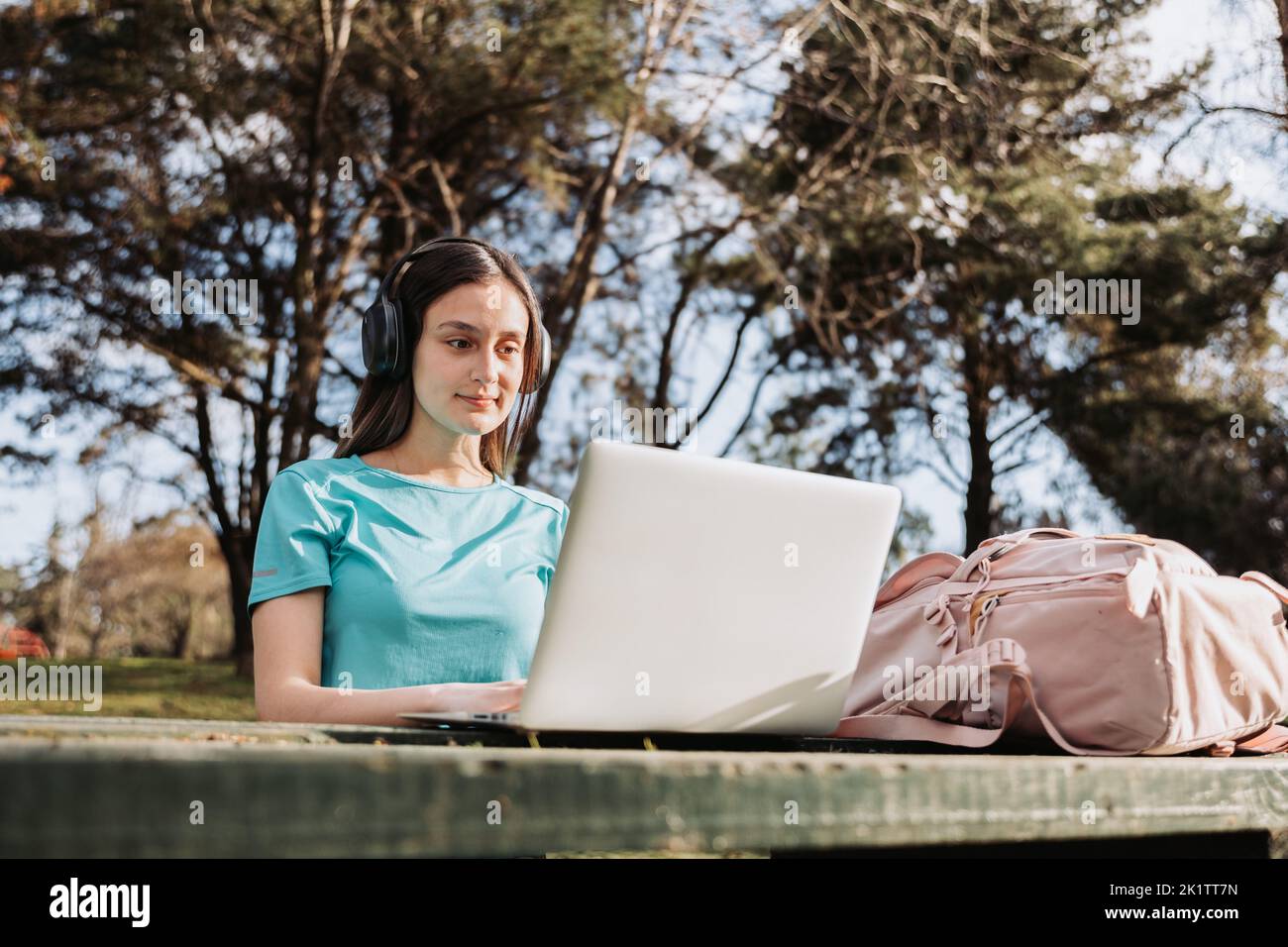Lächelnde Universitätsstudentin, die ihren Laptop im Campus-Naturpark benutzt. E-Learning-Konzept. Stockfoto