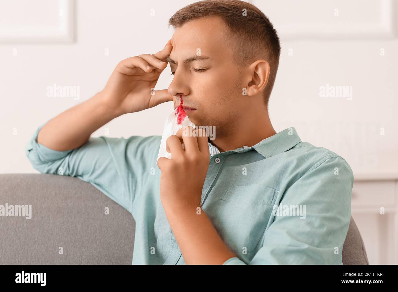 Junger Mann mit Nasenbluten und Gewebe zu Hause Stockfoto