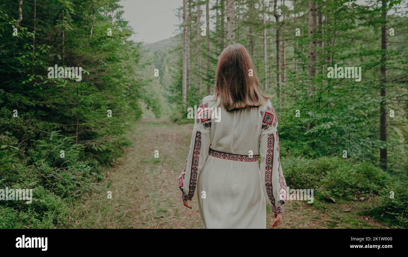 Rückansicht einer unkenntlich ukrainischen Frau, die im Tannenwald, in der Natur der Karpaten spazierengeht. Mädchen in traditionellen Stickerei vyshywanka Kleid Stockfoto