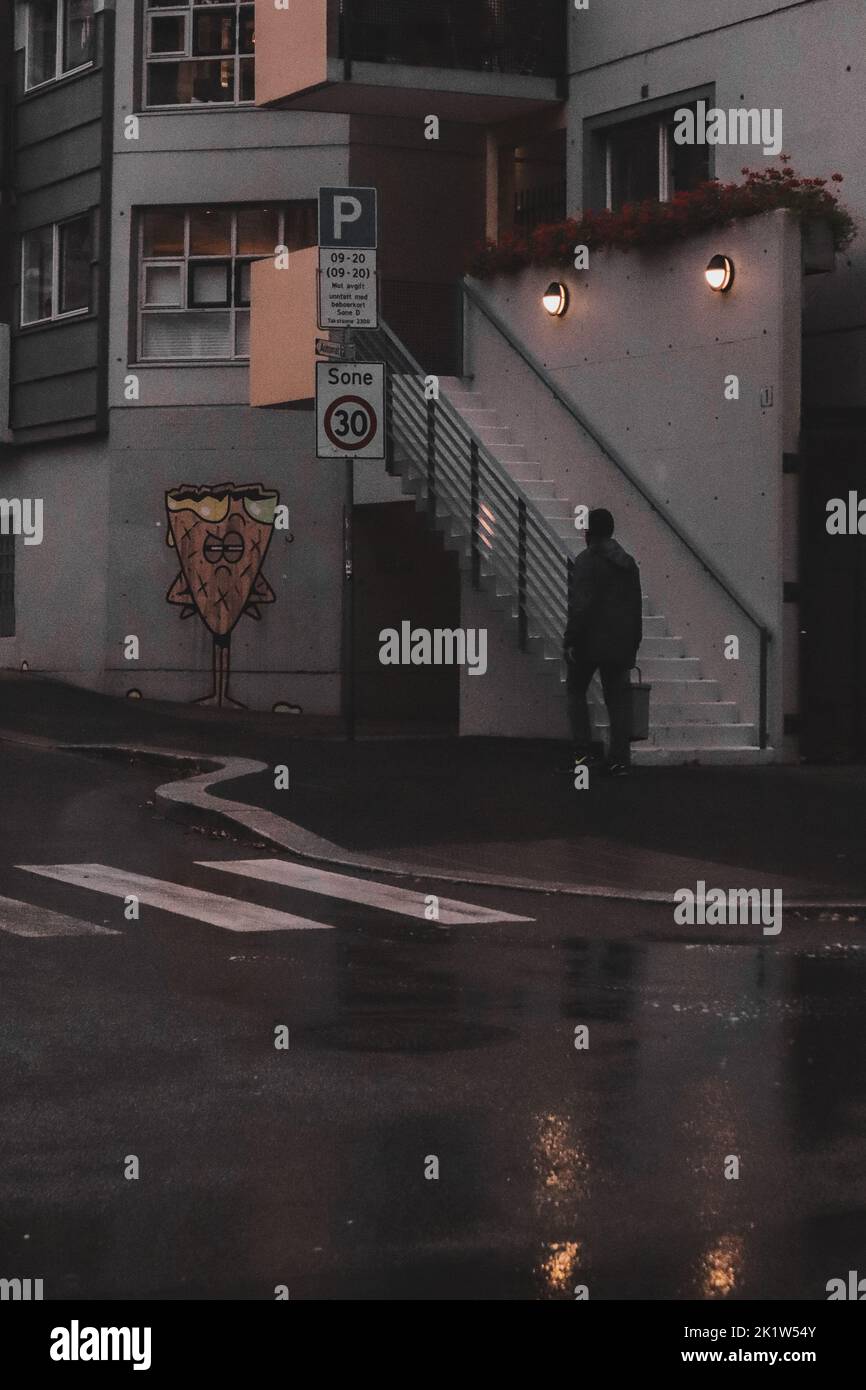 Ein Mann in schwarzer Jacke, der an einer Treppe und einem Graffiti im Regen vorbeigeht Stockfoto
