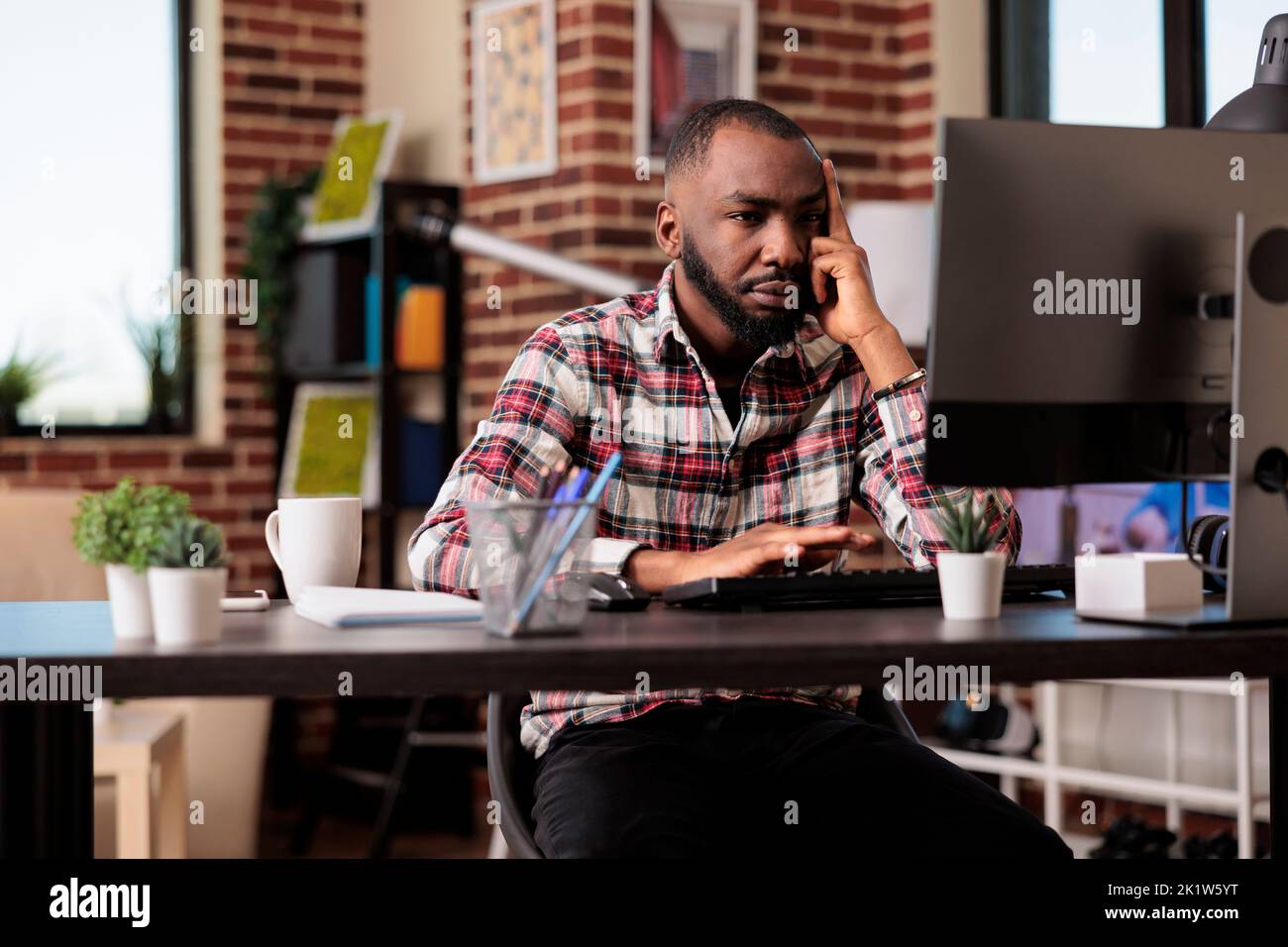 afroamerikanische, müde Angestellte, die an einem Webinar teilnehmen, fühlen sich müde und frustriert über die Remote-Arbeitsbelastung am Computer. Gestresste, erschöpfte Person, die freiberuflich von zu Hause aus arbeitet und unglücklich ist. Stockfoto