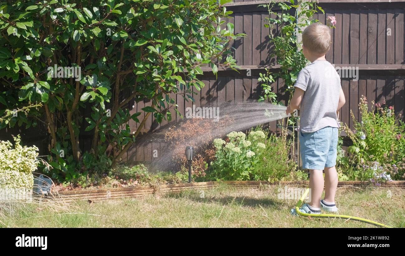 Lustige kleine Junge Bewässerung Rasenpflanzen im Garten Gehäuse