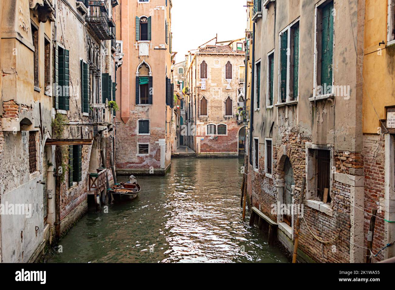 Enger Kanal mit mittelalterlichen Gebäuden, Steinsteg und Brücke, die sich an sonnigen Tagen in Venedig, Italien, in ruhigem Wasser spiegeln. Stockfoto