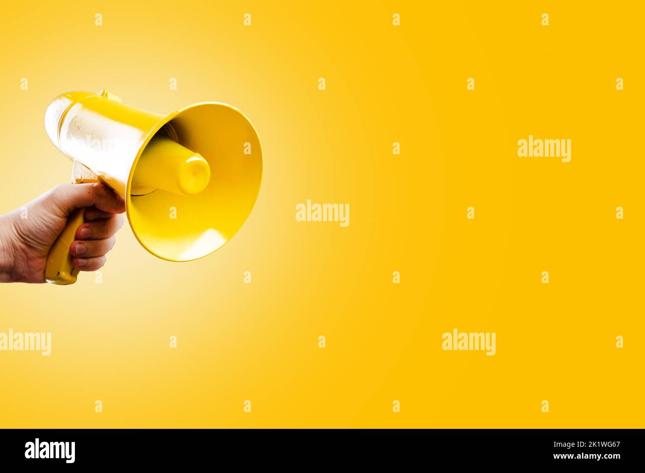 Auf einem leuchtend gelben Hintergrund befindet sich ein gelbes Megaphon in der Hand einer Person. Symbol für falsche Informationen, Gerüchte, Fälschungen. Wahldebatten, Propaganda Stockfoto