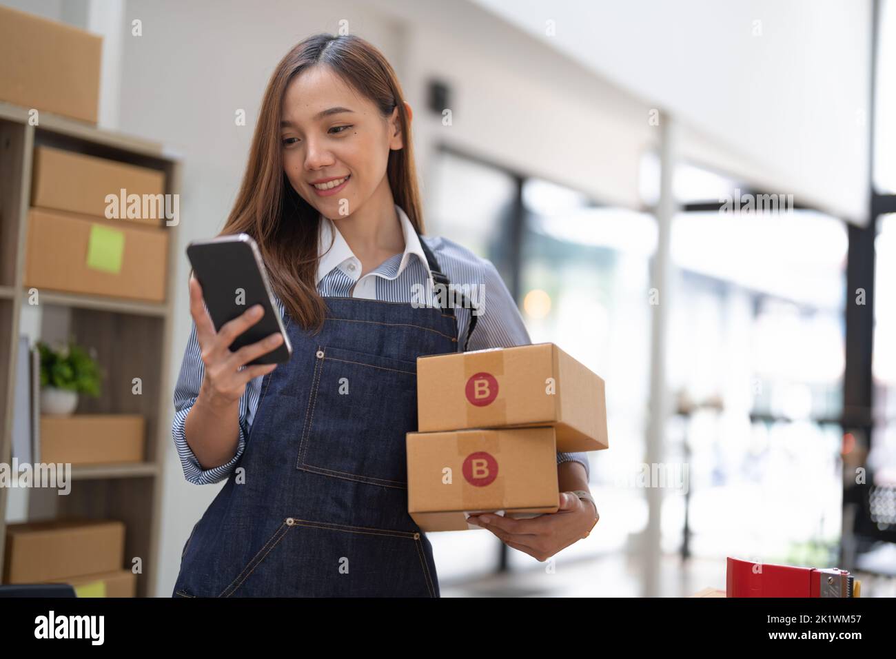 Inhaber eines Kleinunternehmens, das Telefon- und Paketboxen für den Einzelhandel hält und die kommerzielle Versandbestellung über die mobile App auf dem Smartphone überprüft Stockfoto