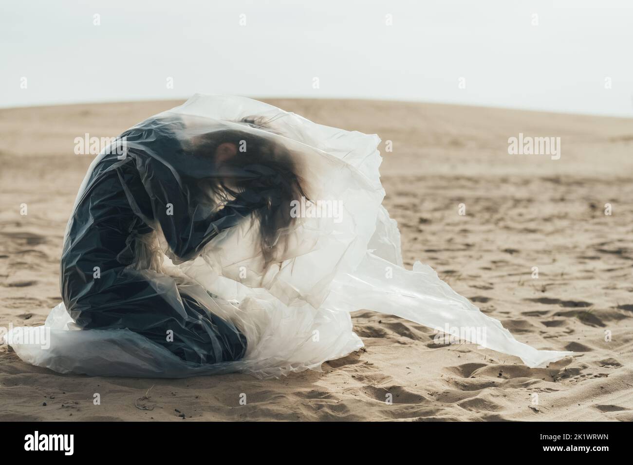 Weibliches Leid. Unschärfende Silhouette. Isolation Einsamkeit. Profil der depressiven Frau in schwarz sitzen auf den Knien umklammenden Kopf in Polyethylen-Film fliegen Stockfoto