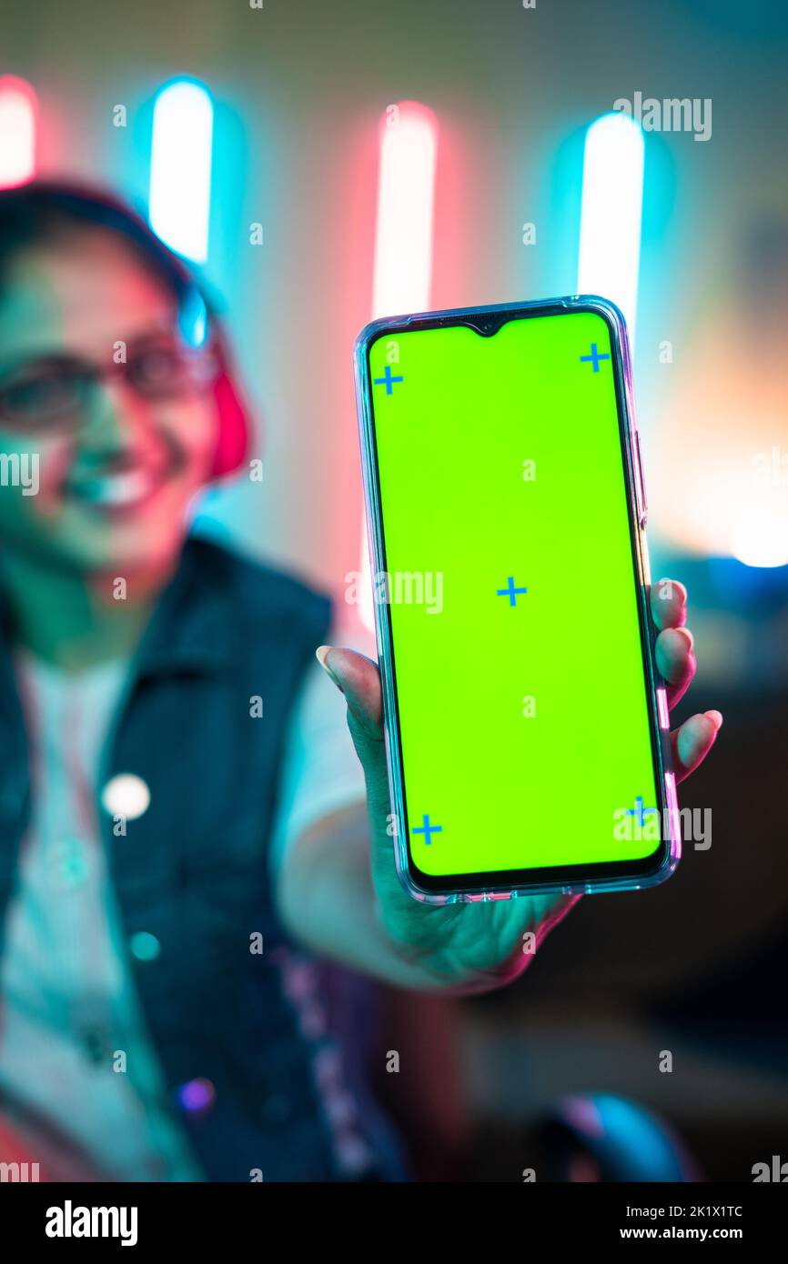 Konzentrieren Sie sich auf Handy, lächelndes Mädchen zeigt grünen Bildschirm Handy, indem Sie Kamera auf Neon-Gaming-Hintergrund. - Konzept der Gaming-Werbung Stockfoto
