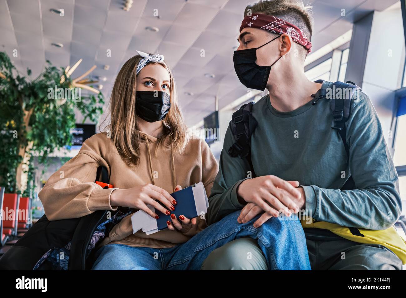 Junge, stilvolle Touristen sitzen am Flughafen mit Pässen in den Händen. Kaukasischer Mann und Frau warten auf ihren Flug zu einem anderen Stockfoto