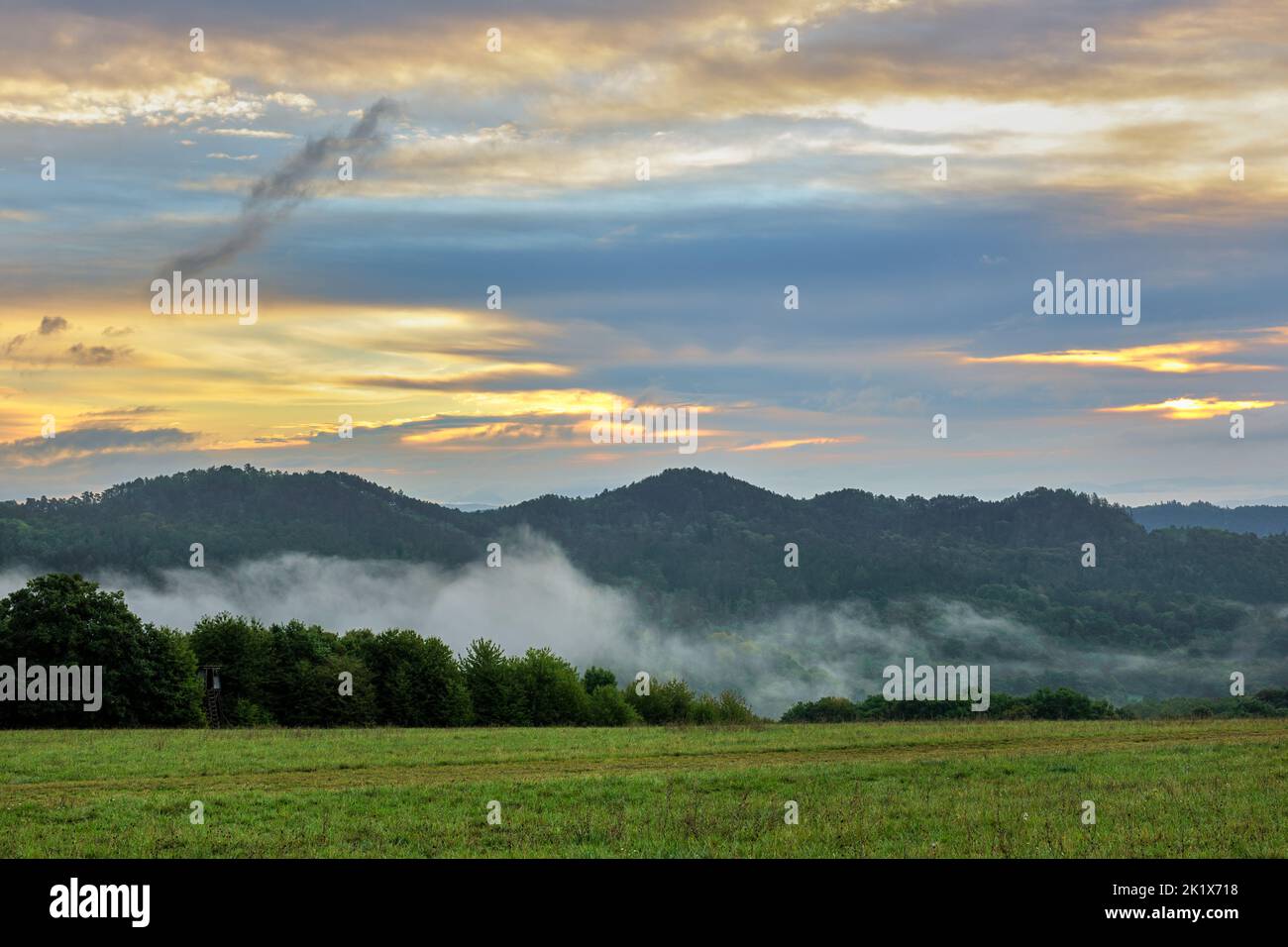 Sonnenaufgang über nebliger Landschaft mit Wald. Nebliger Morgen, bunte Wolken am blauen Himmel. Sommer Natur Europas. Vrsatec, Slowakei. Stockfoto