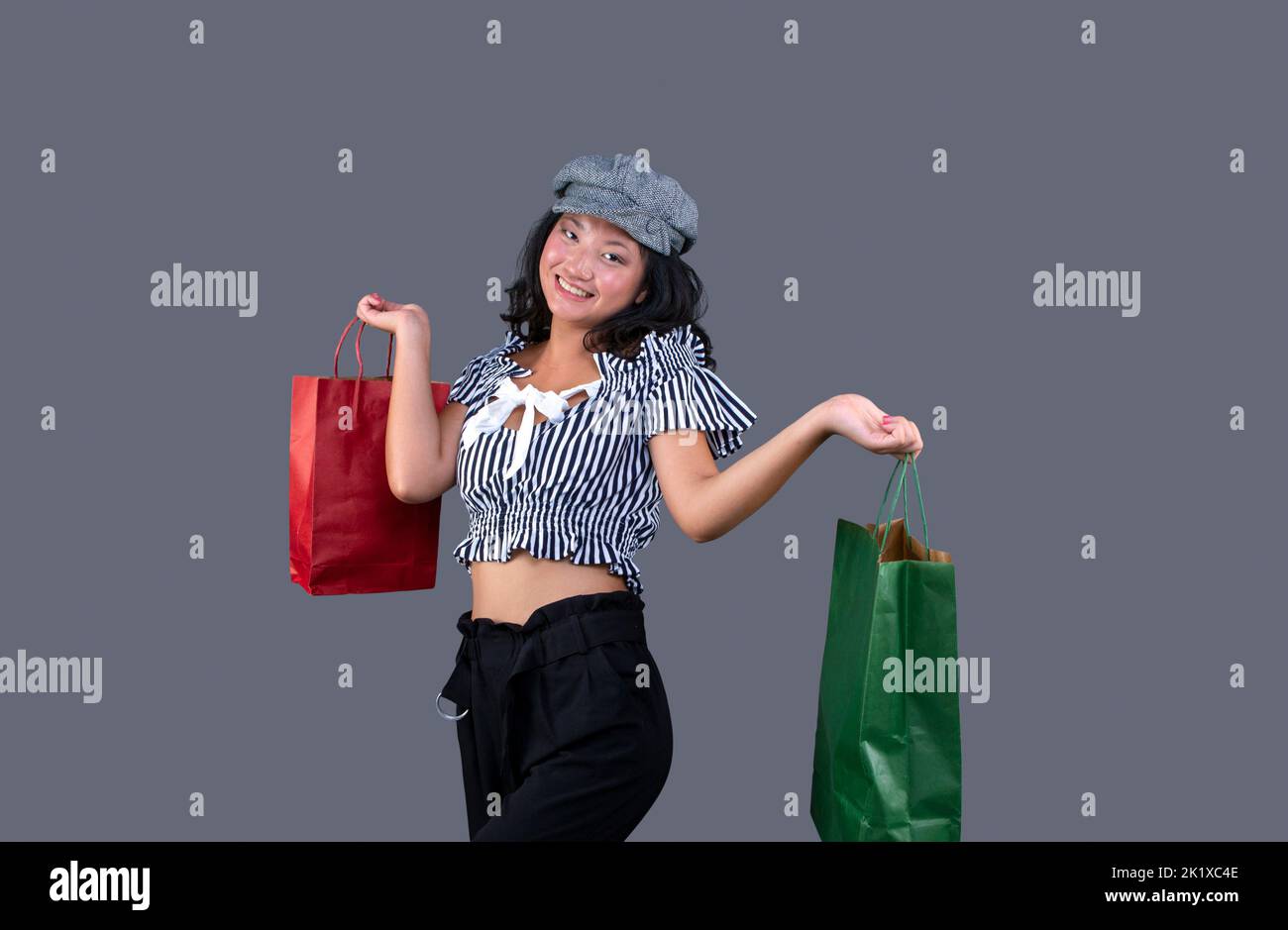 asiatische ethnische Frau mit Einkaufstaschen isoliert auf grauem Hintergrund Stockfoto