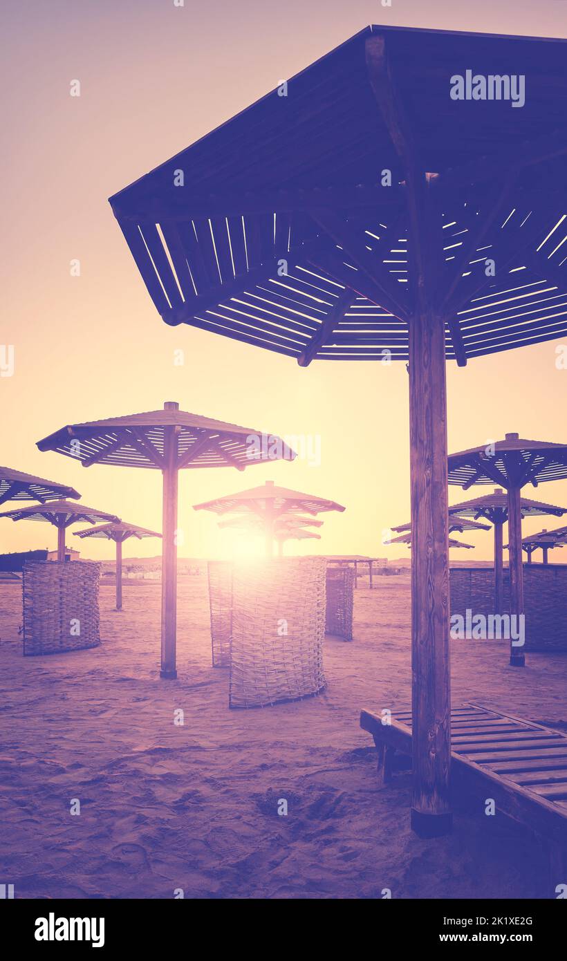 Silhouetten von Sonnenschirmen und Windschutzscheiben am Strand bei Sonnenuntergang, Farbtonung angewendet. Stockfoto