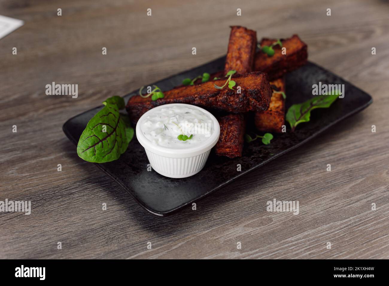 Leckere, würzige Schwarzbrotcroutons mit Knoblauchsauce, Salz und Basilikum auf schwarzem Teller auf Holztisch im Café. Junk Food Stockfoto