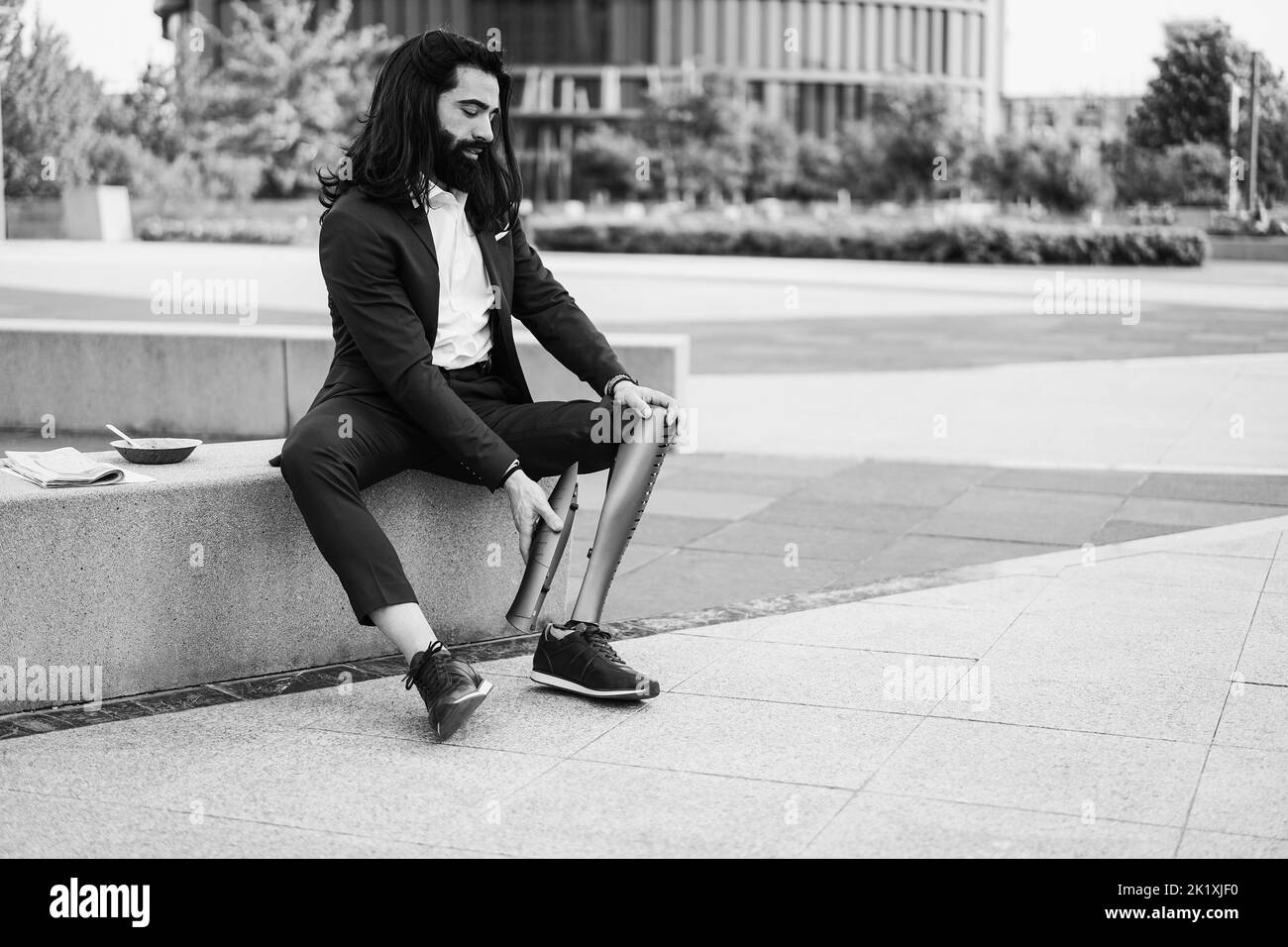 Geschäftsmann, der sein prothetisches Bein im Freien vom Bürogebäude aus anpasst - Fokus auf Hände, die Prothesen halten - Schwarz-Weiß-Schnitt Stockfoto