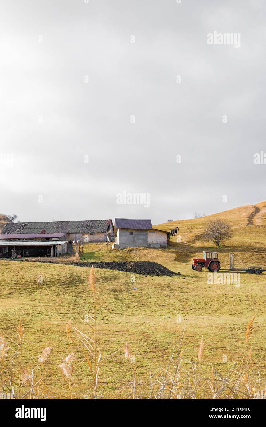 Eine vertikale Aufnahme eines roten Traktors auf einem Grasfeld und von Gebäuden im Hintergrund Stockfoto