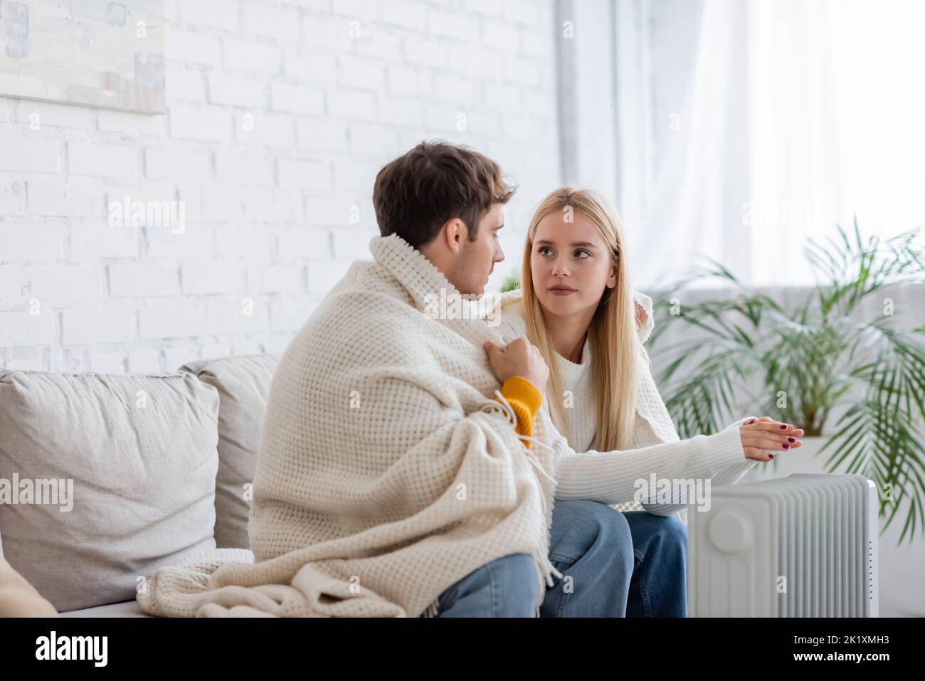 Junges Paar mit Decke bedeckt, sitzt auf der Couch und wärmt sich in der Nähe des Heizkörpers zu Hause, Stockbild Stockfoto