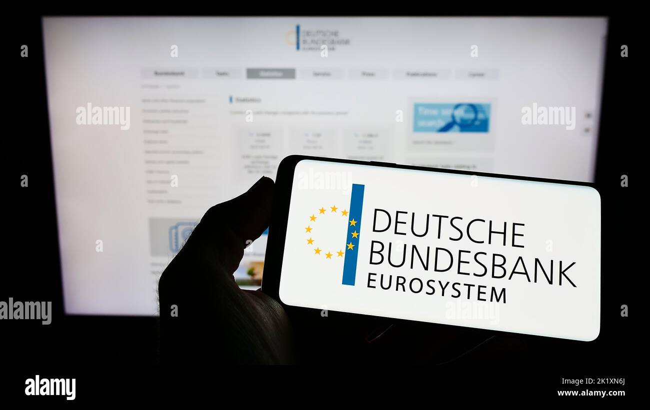 Person mit Mobiltelefon und Logo der Deutschen Bundesbank auf dem Bildschirm vor der Webseite. Konzentrieren Sie sich auf die Telefonanzeige. Stockfoto