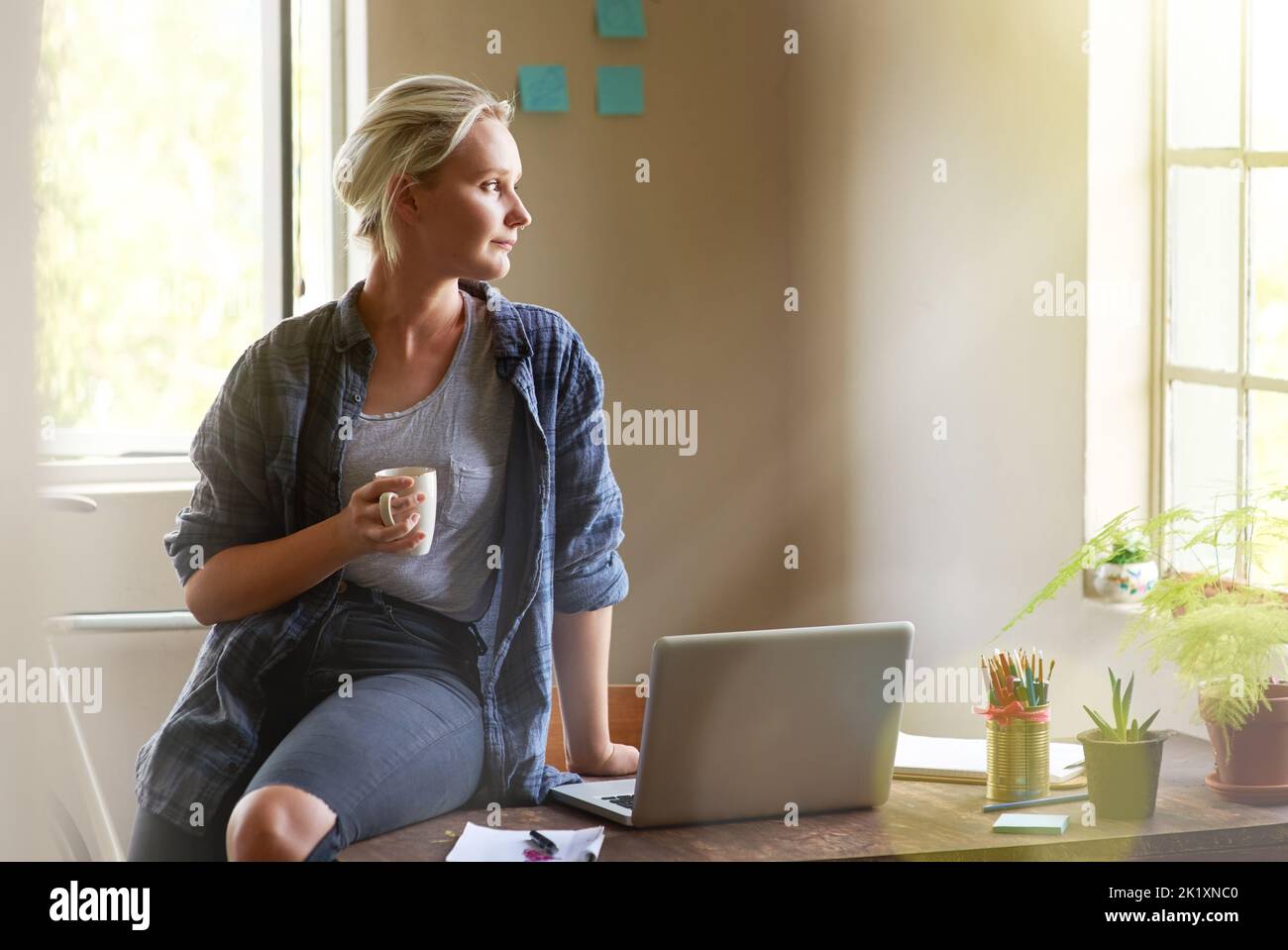 Stellen Sie sich die Möglichkeiten vor... eine junge Frau, die nachdenklich aussieht, während sie auf ihrem Schreibtisch sitzt und Kaffee trinkt. Stockfoto