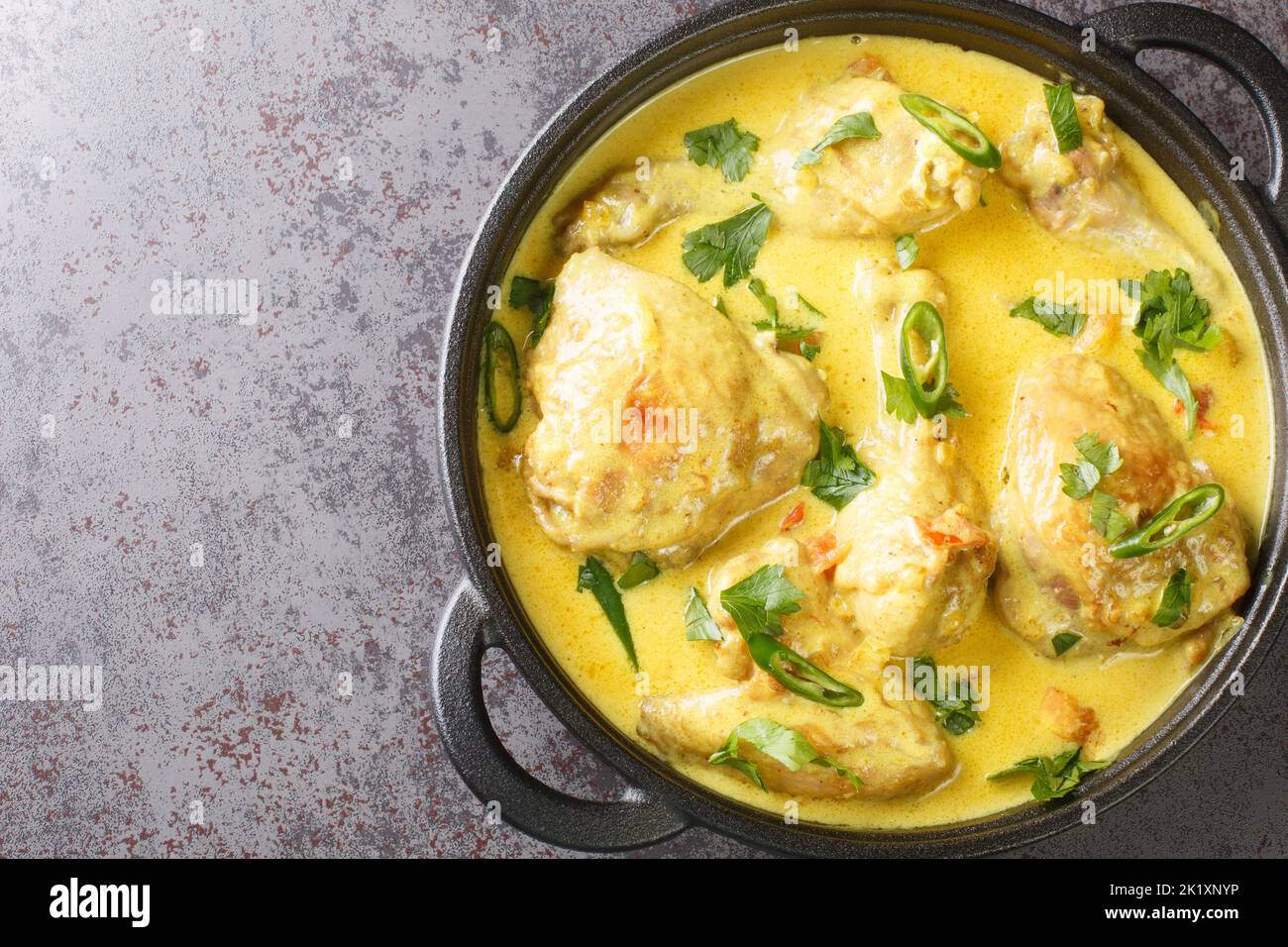 Hühnerstücke in Kokossauce mit Gewürzen, Tomaten, Knoblauch, Zwiebel und Chilischote aus der Nähe in einer Pfanne auf dem Tisch geschmort. Horizontale Ansicht von oben Stockfoto