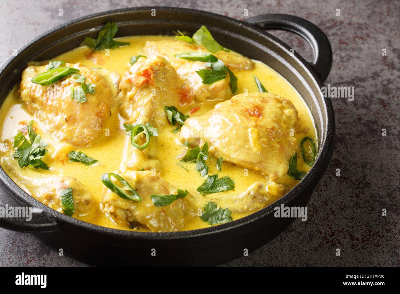 Hühnerstücke in Kokossauce mit Gewürzen, Tomaten, Knoblauch, Zwiebel und Chilischote in einer Pfanne auf dem Tisch geschmort. Horizontal Stockfoto