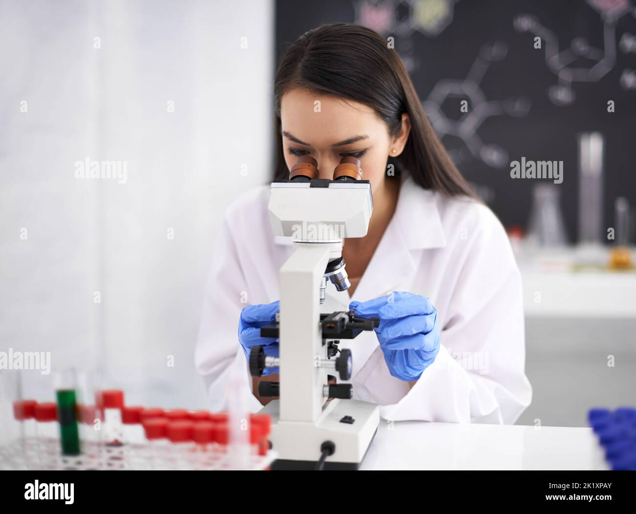 Ein genauerer Blick auf die Probe. Profil einer Wissenschaftlerin, die eine Probe durch ein Mikroskop betrachtet. Stockfoto