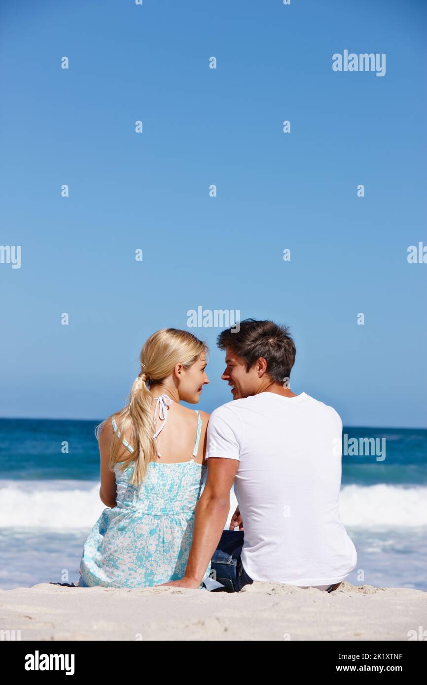 Ich habe nur Augen für dich. Rückansicht eines liebevollen Paares, das am Wasserrand sitzt. Stockfoto