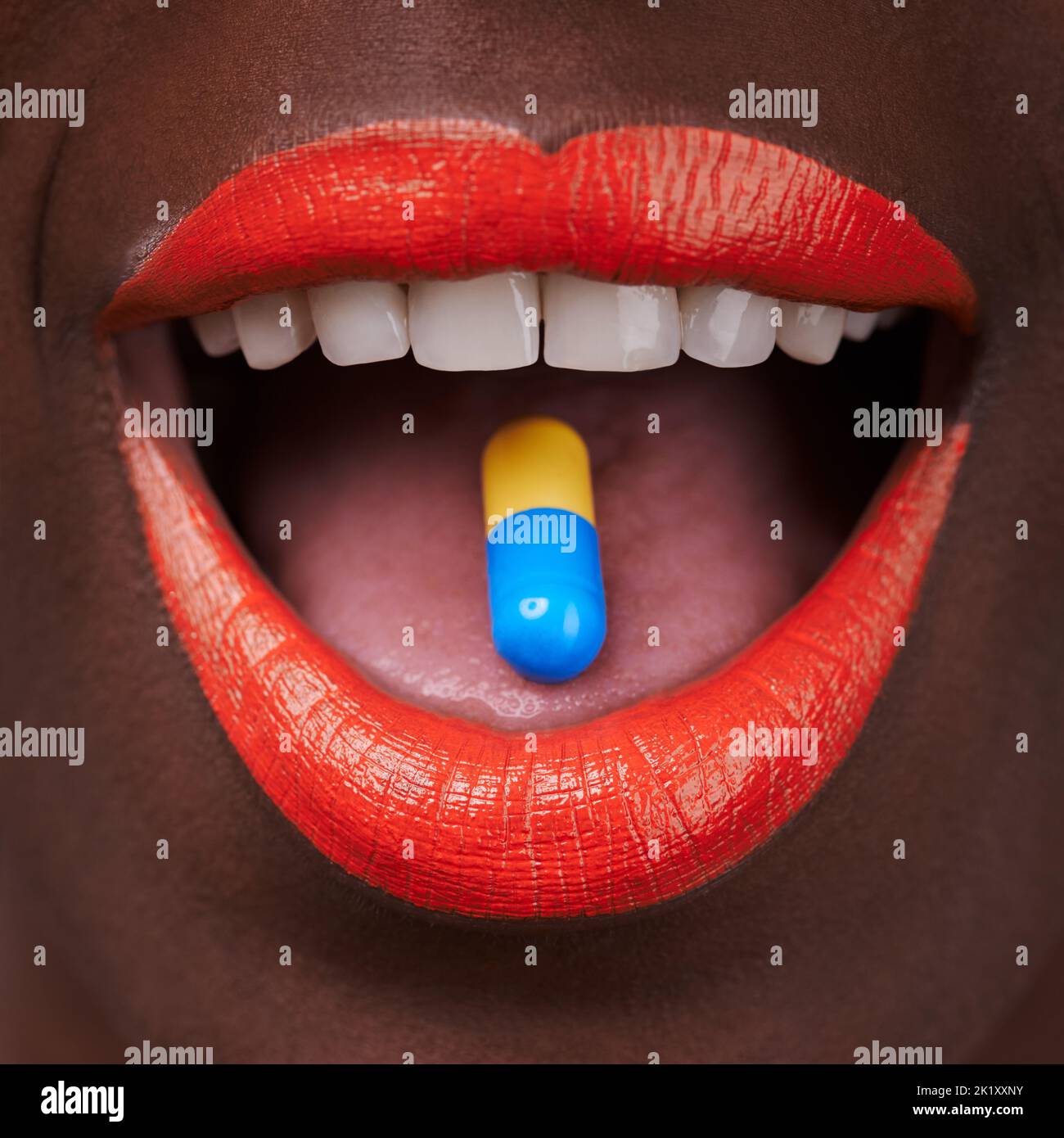 Verleihen Sie Ihrer Welt Farbe. Beschnittene Ansicht einer afrikanischen Frau mit leuchtend roten Lippen, die eine Pille nimmt. Stockfoto