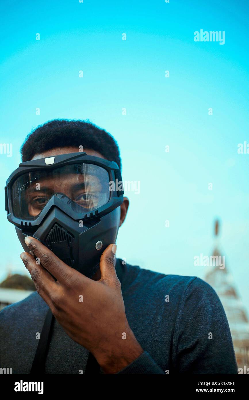 Ein flacher Fokus einer schwarzen Person in einer Goggle-Maske vor einem blauen Hintergrund des Himmels Stockfoto