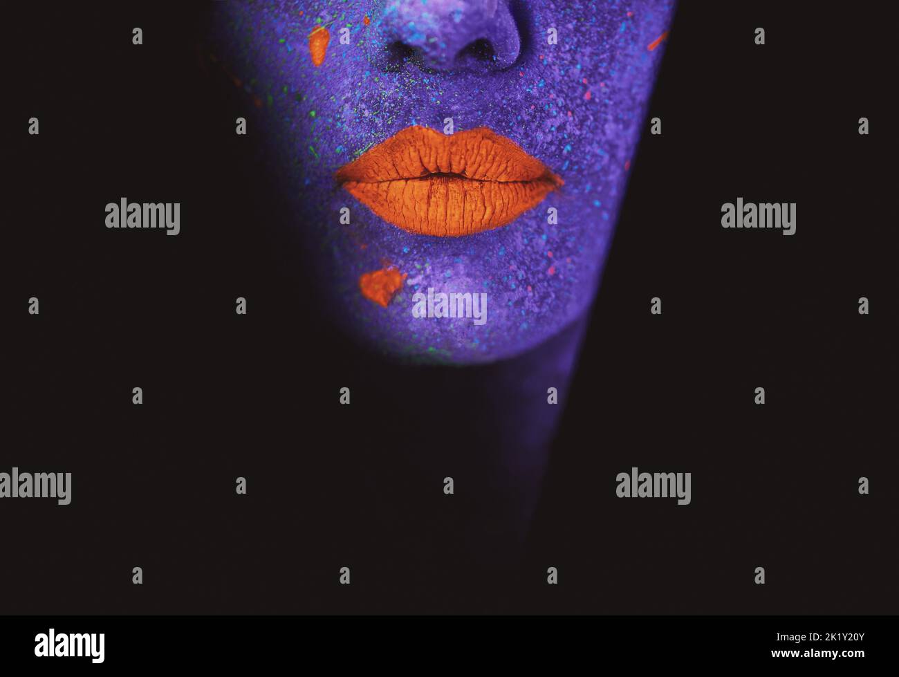Was im Dunkeln geschieht, wird ans Licht kommen. Eine junge Frau posiert mit Neonfarbe auf ihrem Gesicht. Stockfoto