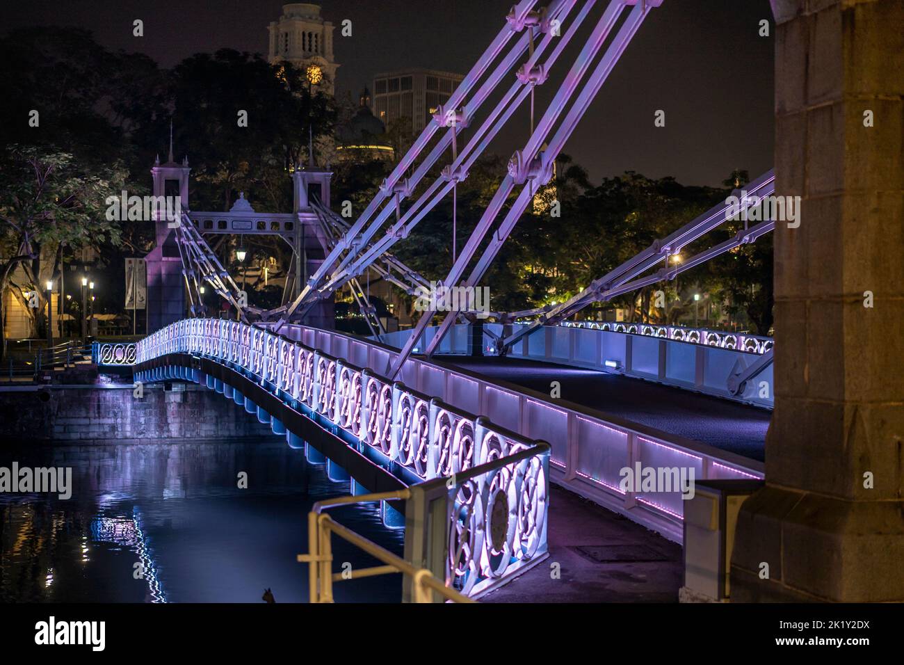 Die Cavenagh Bridge über den Singapore River wird nachts von violetten Flutlichtern beleuchtet. Singapur Stockfoto