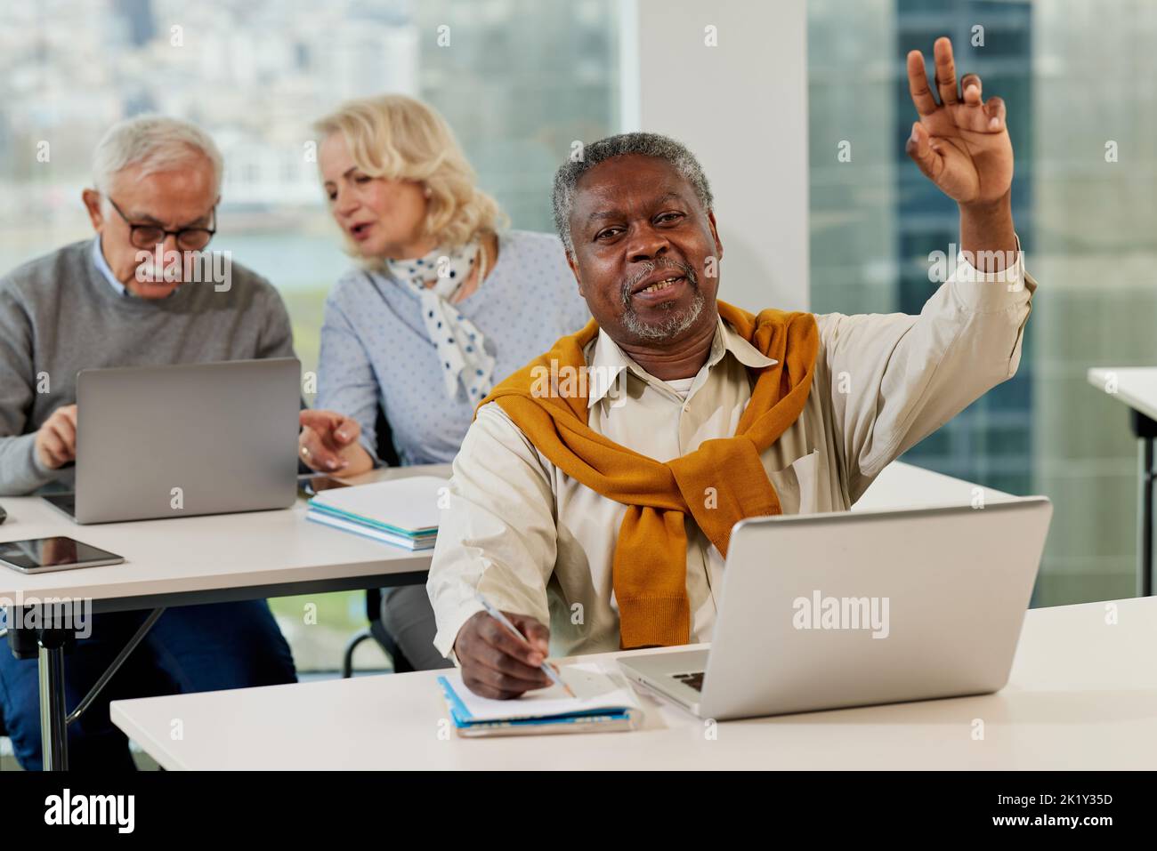 Senioren sitzen in einem Klassenzimmer und reden über das Projekt auf dem Laptop, während ein multikultureller Senior Student im Vordergrund Fragen stellt. Stockfoto