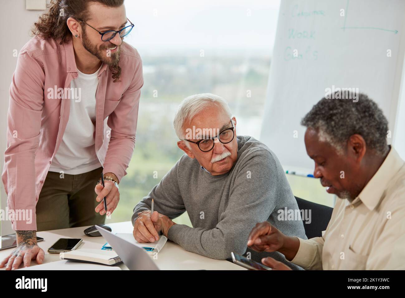 Ein junger Lehrer lehrt eine kleine Gruppe multikultureller älterer Schüler, wie man Technologien nutzt. Stockfoto