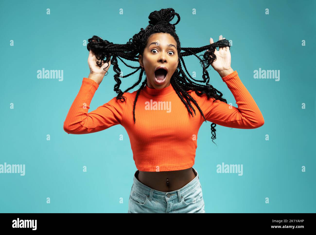 Junge liebenswerte Frau mit afrikanischer Frisur lachend während des Indoor-Fotoshootings. Anmutige niedliche Mädchen in legerer Kleidung genießen Freizeit im Studio. Stockfoto