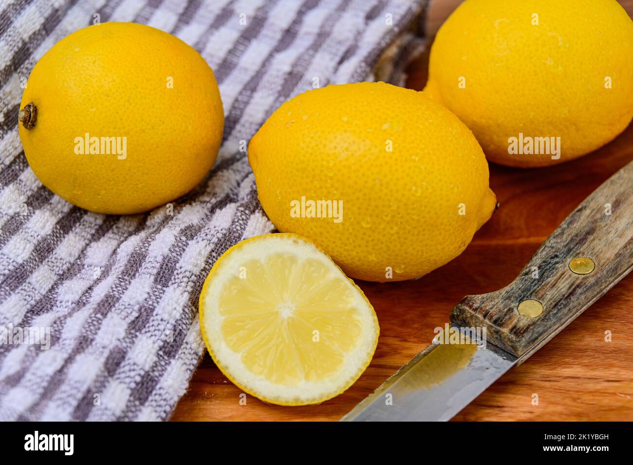 Ganze und geschnittene Zitronen auf einem Tuch und Holzhintergrund mit Schneidemesser Stockfoto