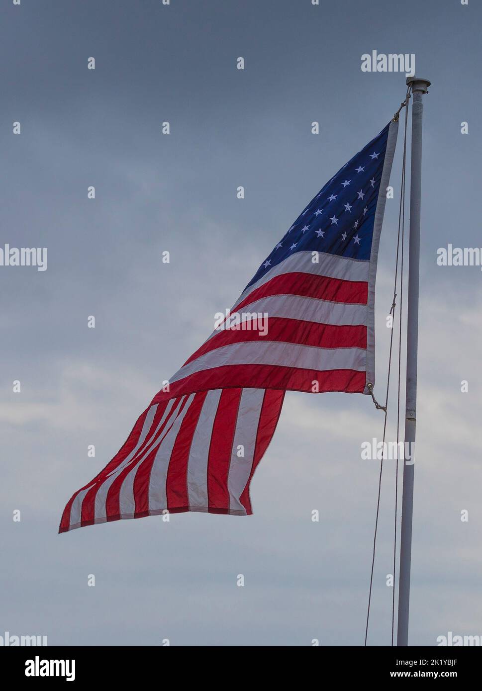 Kleiner Wind, der eine amerikanische Flagge mit Wolken hinter sich faltet Stockfoto