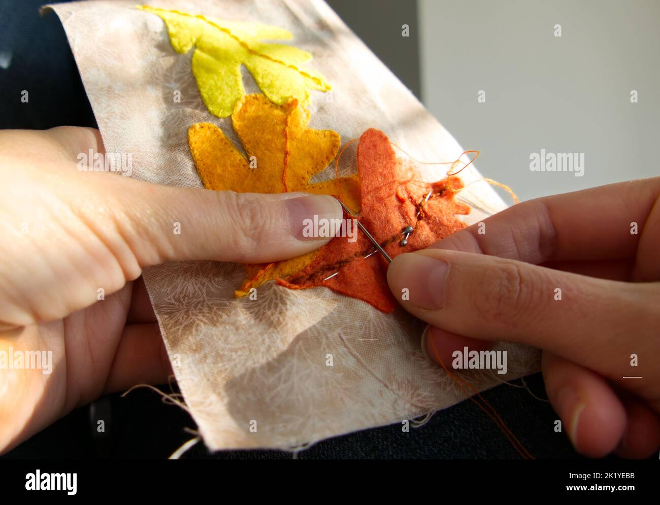 Nahaufnahme der Hände einer Frau, die näht, um appliqué-Arbeiten von Herbstblättern zu produzieren. Stockfoto