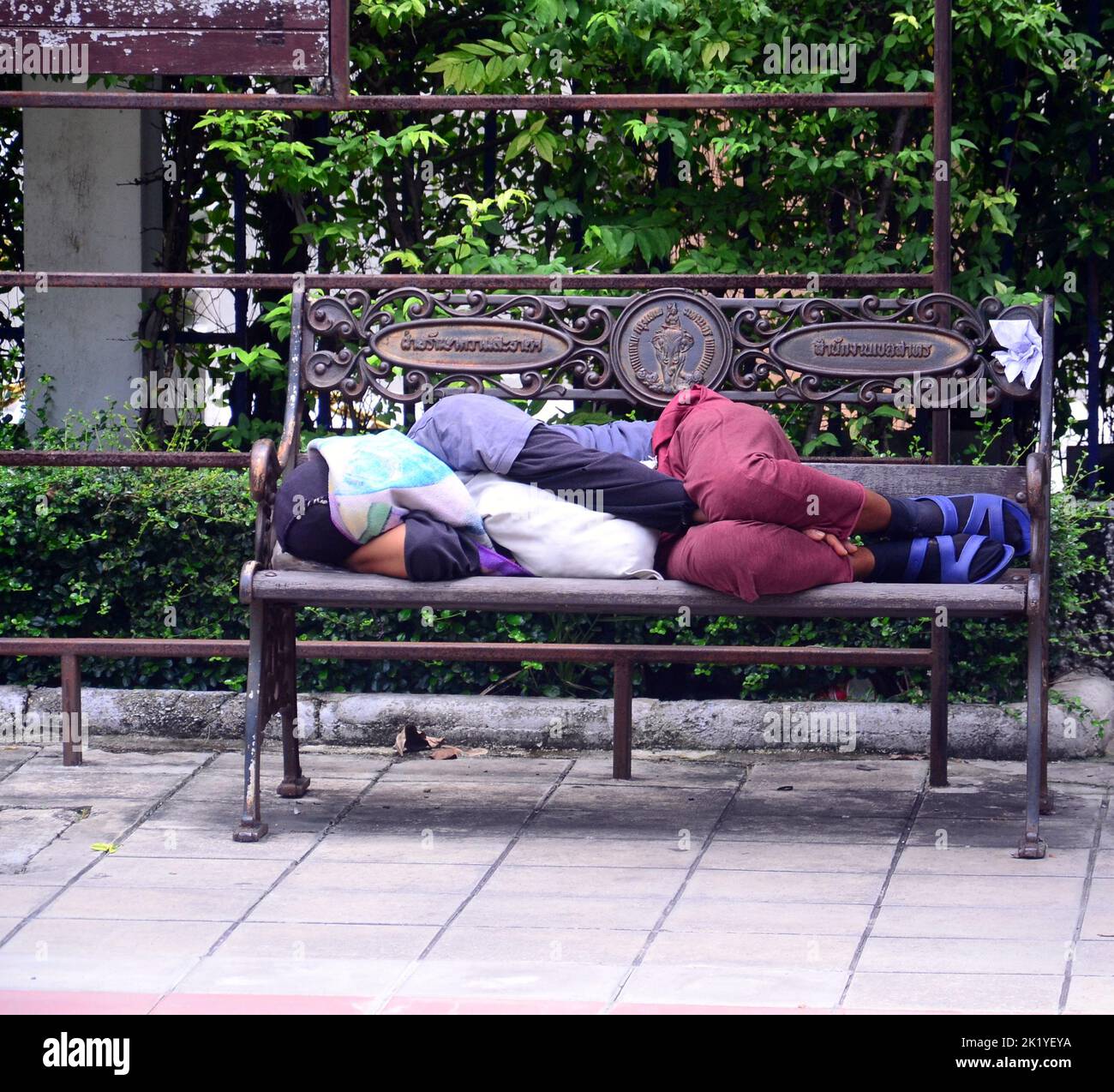 Eine Person schläft tagsüber auf einer Bank auf der Straße in Bangkok, Thailand, Südostasien. Dies ist ein regelmäßiger Anblick in Bangkok, wo die Unterkunft relativ teuer ist im Vergleich zu dem Mindestlohn von etwa $7 pro Tag. Stockfoto