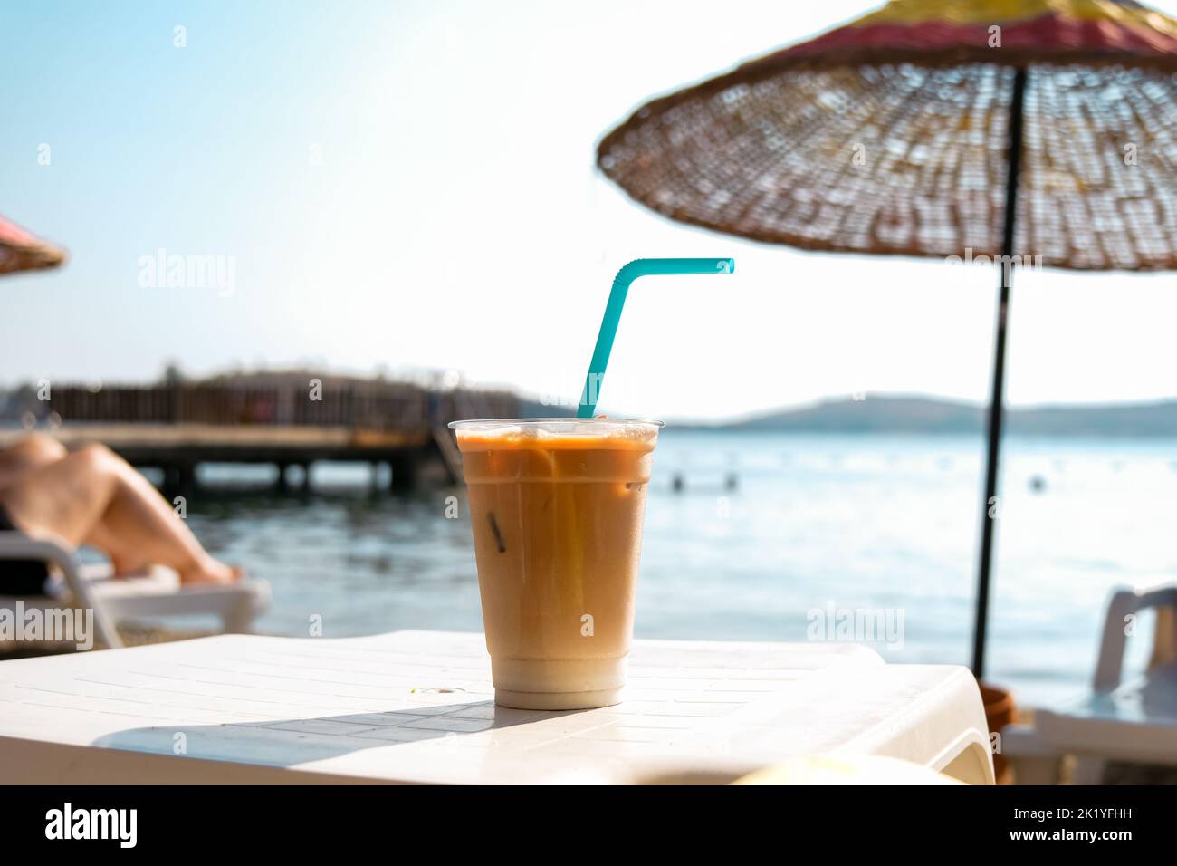 Eis-Latte-Kaffee in Plastikglas am Strand. Stockfoto