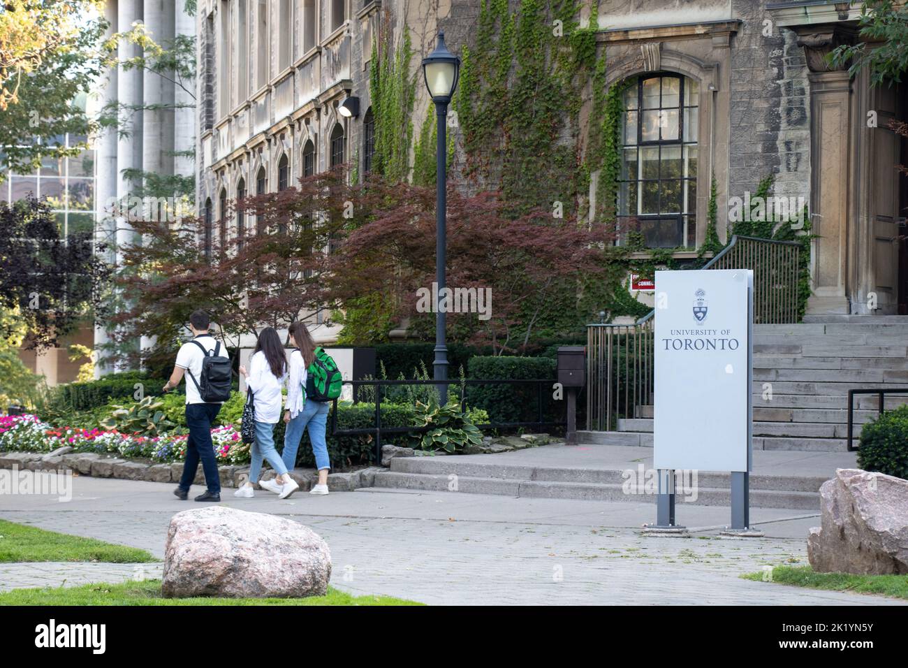 Studenten gehen an einem Gebäude mit einem Schild für die Universität von Toronto vorbei, das an einem sonnigen Nachmittag auf dem Campus zu sehen ist. Stockfoto