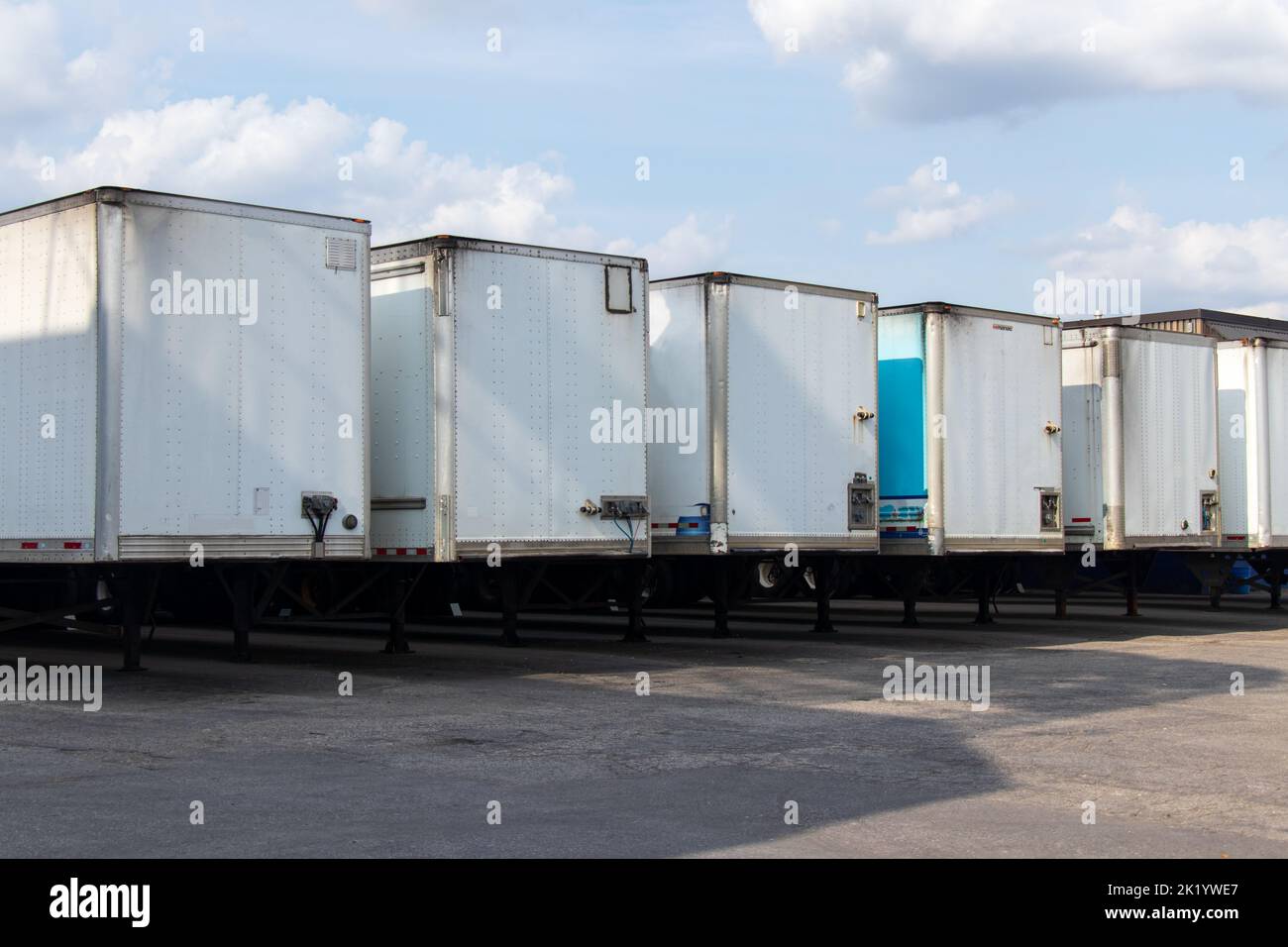 An einem teilweise bewölkten, sonnigen Tag stehen vor einem Lagerhaus eine Reihe weißer Transportanhänger. Stockfoto