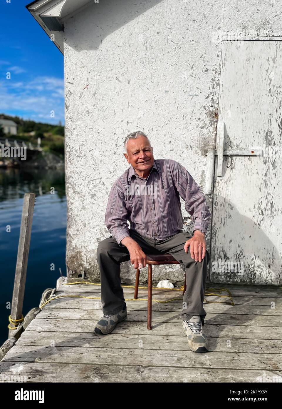 Porträt eines glücklichen älteren Mannes, der auf dem Dock in Neufundland sitzt. Stockfoto