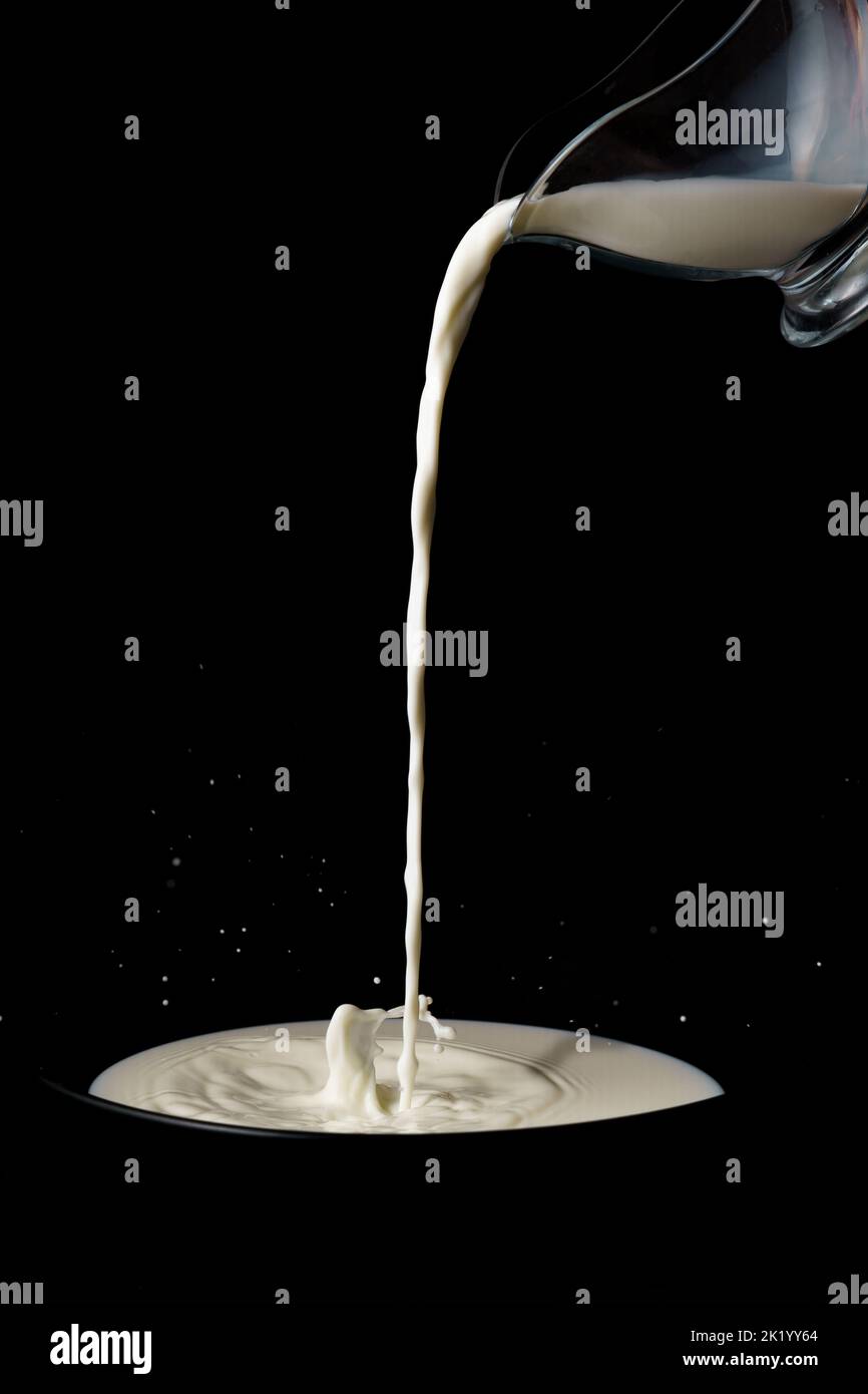 Krug gießt Milch in einen Spritzer-Teller-Effekt Stockfoto