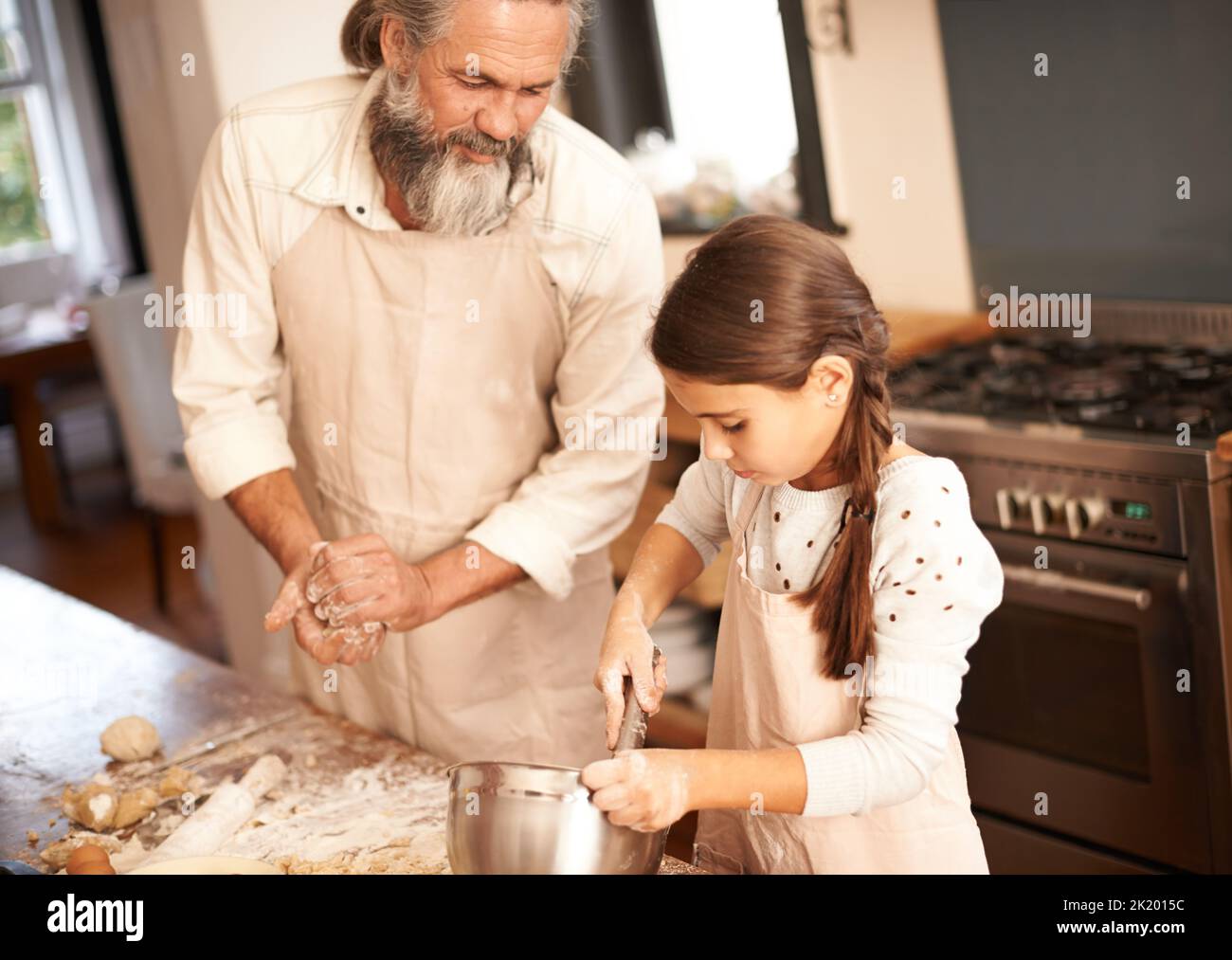 Opa lehrt sie ein oder zwei Dinge. Ein Mädchen, das sich mit ihrem Großvater verklebt, während sie in der Küche backen. Stockfoto