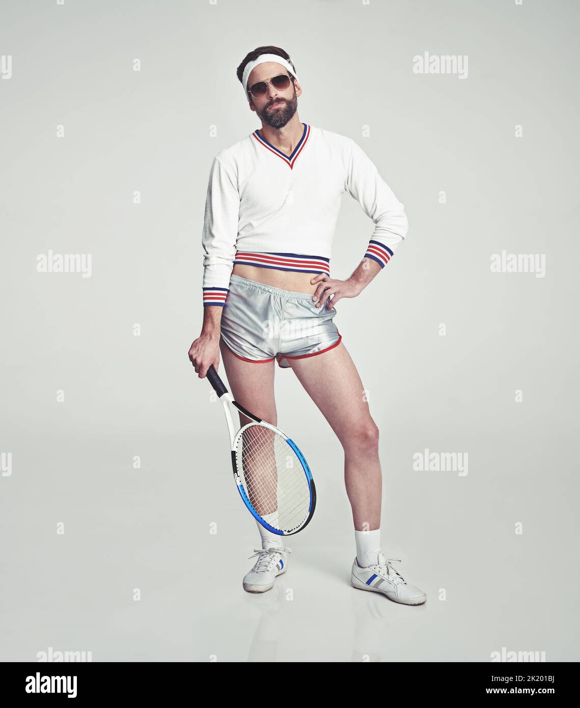 Ist das alles was du hast. Ein junger Mann im Studio, der schlecht sitzende Retro-Tennisbekleidung und -Schirme trägt, während er einen Schläger hält. Stockfoto Ist das alles was du hast. Ein junger Mann im Studio, der schlecht sitzende Retro-Tennisbekleidung und -Schirme trägt, während er einen Schläger hält. Stockfoto