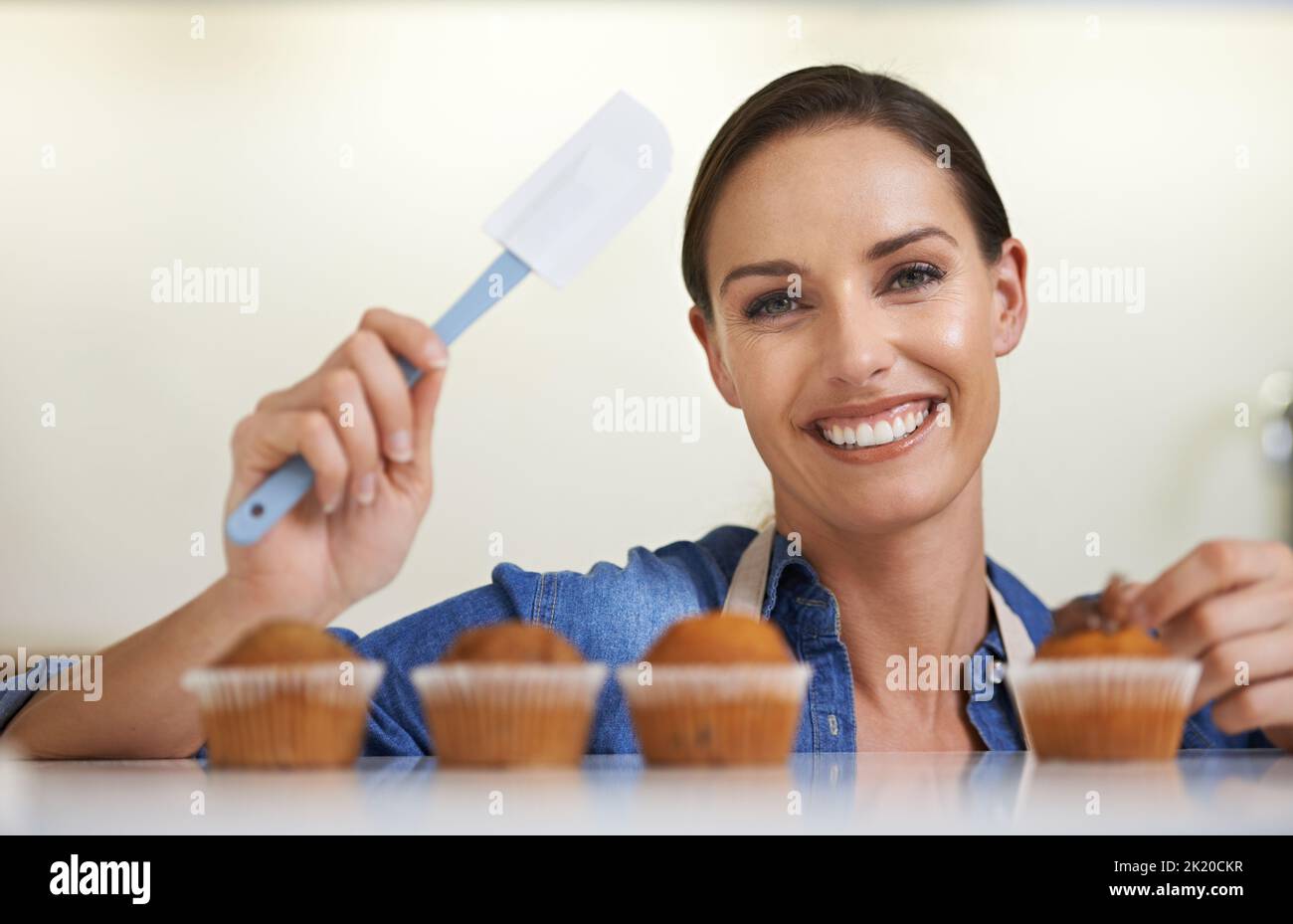 Es ist das Sahnehäubchen auf dem Kuchen. Eine glückliche junge Frau, die gerade dabei ist, ihren frisch gebackenen Cupcakes Zuckerguss zu geben. Stockfoto
