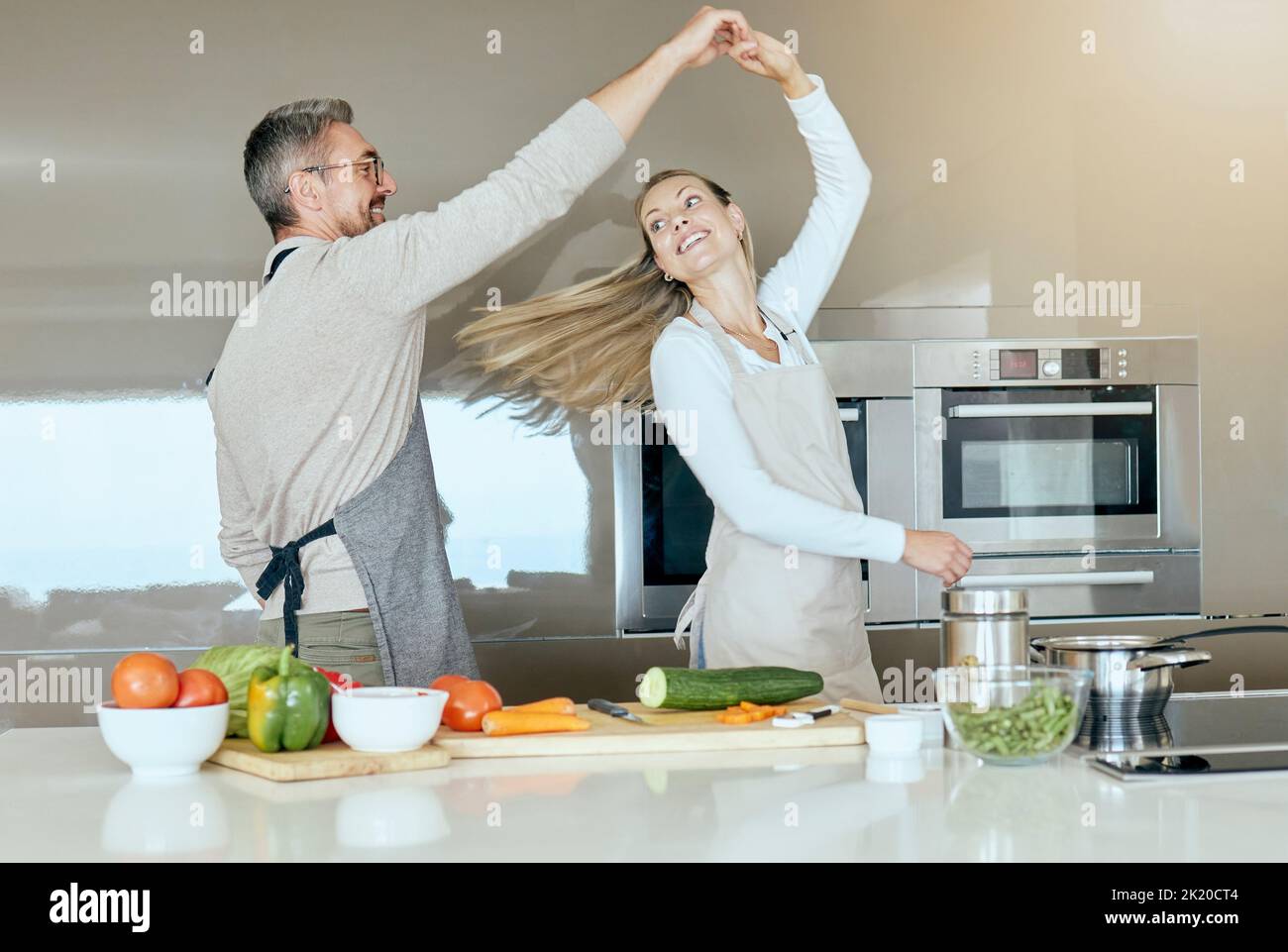 Tanzendes Paar, Kochen und Liebe in der Küche, während Gemüse für eine gesunde, organische und vegane Mahlzeit oder Salat zubereitet wird. Glücklicher Mann und Frau mit Stockfoto